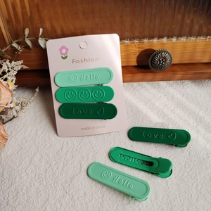 Dettaglio dei fermagli per capelli verdi opachi con scritte Hello e Love su cartoncino