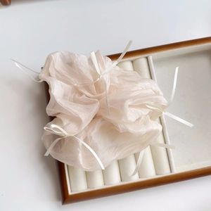 Detail der Textur eines champagnerfarbenen Organza-Scrunchie mit kleinen weißen Schleifen