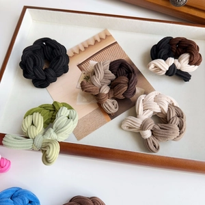 Detail view of woven fabric elastic hair ties in earth-toned colors on a wooden tray