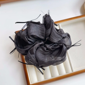 Detailansicht eines schwarzen Organza-Haargummis mit Satinschleifen auf einem Holztablett