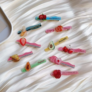 Close-up of glitter acrylic fruit hair clips on silk fabric featuring cherry and strawberry