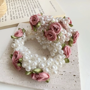 Detail von elegantem Perlen-Haargummi mit rosa Satinrose und Blatt auf Stein