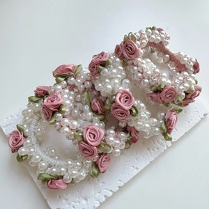 Detailansicht von Haargummis mit rosa Satinrosen, eleganten Perlen und grünen Seidenblättern