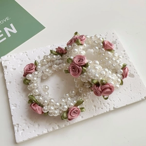 Detail von Perlenhaargummis mit handgefertigten rosa Bandrosen und grünen Blättern