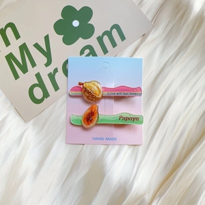 Detailed macro of glitter acrylic durian and papaya hair clips on a soft fabric