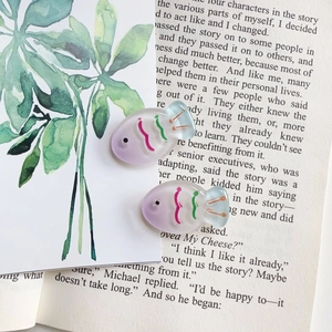 Macro detail of gradient fish-shaped resin hair clips on a decorative book background