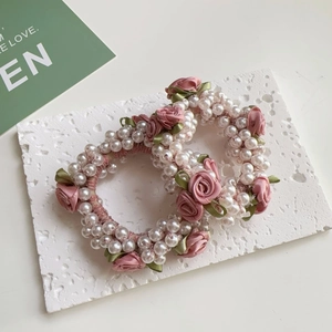 Detail eines Perlen-Haargummis mit rosa Seidenrose und grünen Blättern auf Steingrund