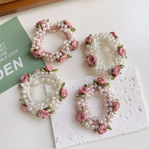 Detailsicht von vier Perlenhaargummis mit rosa Satinrosen und grünen Schleifenblättern