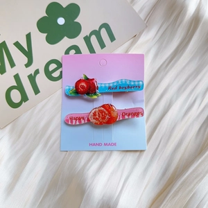 Detail view of handmade acrylic hair clips with berry and orange designs on a card