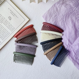 Nine colorful matte hair side combs arranged on a textured white base with a book