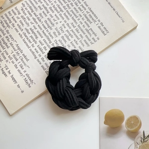 Detailed view of a black braided elastic hair tie with a chic bow on a book background