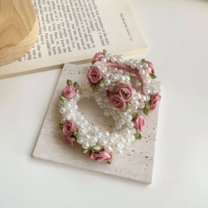 Detaillierte Makroaufnahme von weißen Perlen-Haargummis mit kleinen rosa Stoffrosen und Blättern