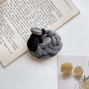 Close-up of thick gray and black braided elastic hair tie on a soft aesthetic background