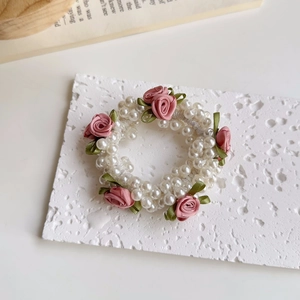 Nahaufnahme von rosa Satinrosen und Kunstperlen auf einem eleganten Haargummi