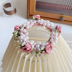 Detail von rosa Stoffrosen und Kunstperlen auf einem eleganten Vintage-Haargummi