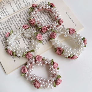 4er-Set elegante Perlen-Haargummis mit rosa Stoffrosen auf Vintage-Buch Hintergrund