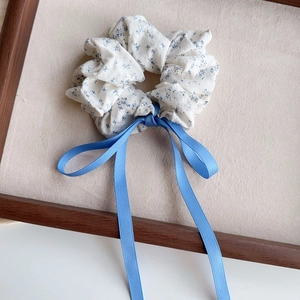 Macro detail of a sea salt blue floral scrunchie with a navy ribbon bow on a wooden display