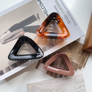 Detailed close-up of large triangular hair claw clips in amber, black, and brown finishes