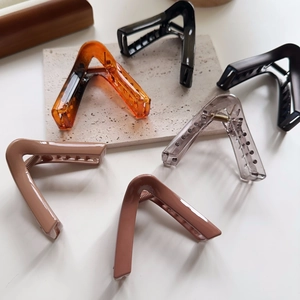 Macro shot of triangular hair claw clips in neutral resin shades on a stone platform