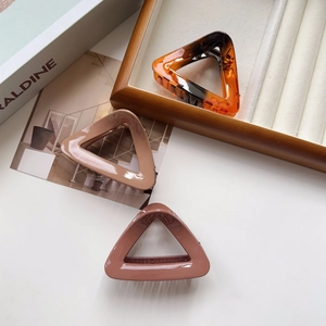 Close-up of three triangle hair claw clips in amber, beige, and dusty pink on a tray