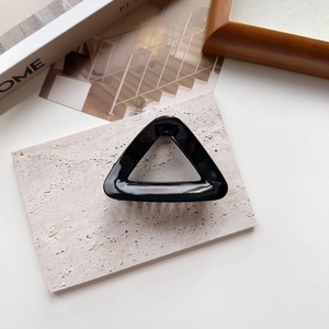 Detail of a black triangular hair claw clip with glossy finish on a grey stone tray