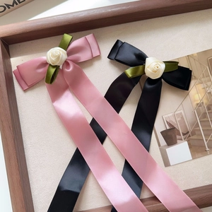 Detail of pink satin bow hair clip with white rose floral centerpiece and long ribbons