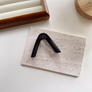 Detail shot of a matte black triangular hair claw clip on a minimalist stone display