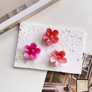 Flat lay of three floral hair claws in red, magenta and pink gradient on a white surface