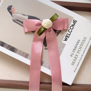 Detail of pink satin bow hair clip with cream silk rose and long elegant ribbons