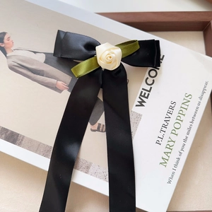 Detail of a handmade black satin bow hair clip with a cream rose and long ribbons