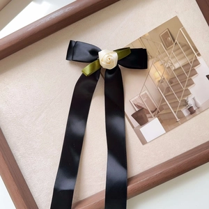 Detail of elegant black satin ribbon bow with a cream fabric rose and green leaves