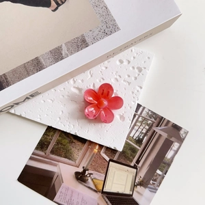 Detailed view of a coral pink floral claw clip on a textured decorative white surface