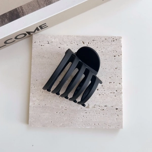 Détail d'une grande pince à cheveux noir mat avec design multi-dents sur surface pierre