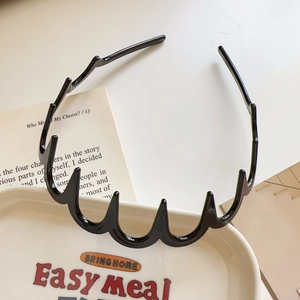 Close-up of a glossy black wavy tooth headband resting on a minimalist ceramic plate