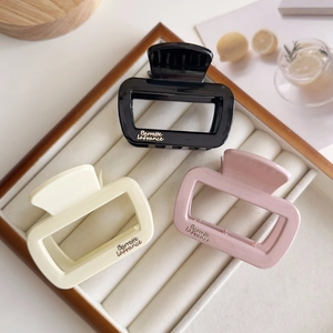 Détail de trois pinces à cheveux carrées noir crème et rose sur un plateau en velours