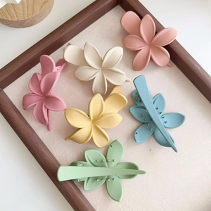 Détail de pinces à cheveux fleurs mates aux tons pastel sur un plateau en tissu beige