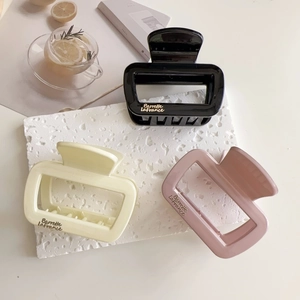Détail de pinces à cheveux rectangulaires évidées en noir, crème et rose avec lettrage doré