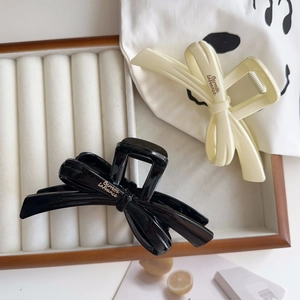 Close-up of black and cream resin hair claws with ribbon bow design and branding