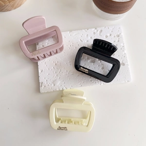 Gros plan de trois pinces à cheveux carrées en rose, noir et beige, fini brillant