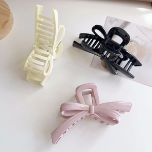 Elegant ribbon bow hair claws in cream, black, and pink colors on a white background