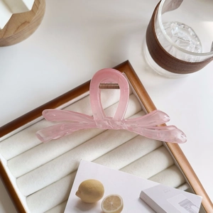 Détail d'une pince à cheveux rose translucide en forme de nœud sur un plateau en velours