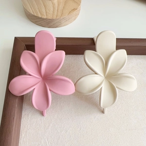 Détail de pinces à cheveux fleurs mates en rose et crème sur un cadre en bois