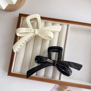 Elegant ribbon bow hair claw clips in cream and black resin on a jewelry display tray