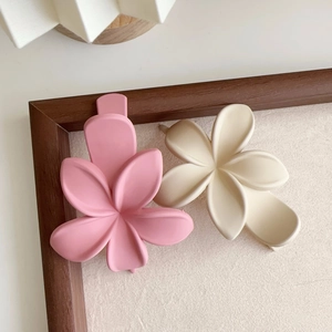 Détail de pinces à cheveux fleur de frangipanier mate en rose et crème sur fond de toile