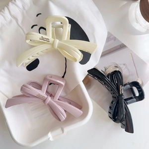 Detail of elegant bow hair claws in cream, pink, and black with gold logo lettering