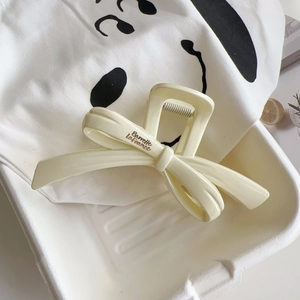 Close-up of a cream bow hair claw clip with golden French lettering on a white surface