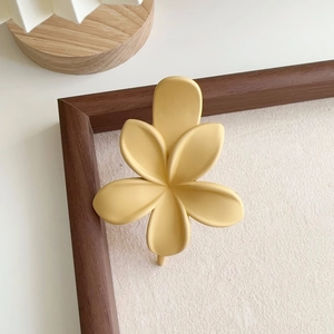 Détail d'une pince à cheveux fleur mate jaune au design frangipanier sur fond blanc