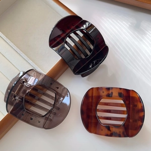 Detailed view of three large tortoiseshell and matte hair claws on a white wooden surface