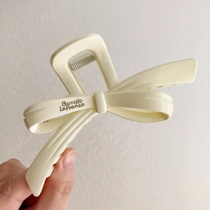 Detailed view of cream bow hair claw clip with engraved Barrette LaFrance logo