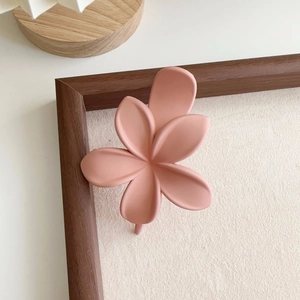 Vue détaillée de dessus d'une pince à cheveux fleur rose mat sur un fond en tissu beige